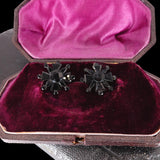 Pair of black star-shaped earrings in an open jewelry box with purple interior.