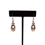 Pair of rose gold earrings on a black earring stand against a white background