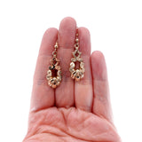 Gold earrings held in a hand on a white background