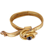 Gold bracelet with a knot design and black gemstone on a white background