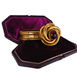 Gold bracelet with a red gemstone in a purple-lined jewelry box on a white background