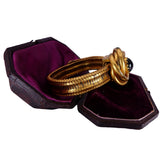 Gold bracelets in a jewelry box with purple lining on a white background