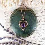 Rose gold necklace with purple gemstone on a green stone, surrounded by white roses and lavender.