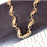 Gold chain necklace on a textured dark surface with text underneath