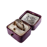 Gold ring in a purple jewelry box with visible branding on a white background