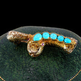 Gold brooch with turquoise stones on a dark green cushion