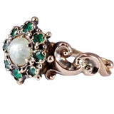 Rose gold ring with pearl and emeralds on a white background
