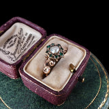 Vintage brooch with green gemstones and pearl in a purple jewelry box on a green surface.