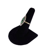 Ring with green gemstone and gold band on a black velvet stand against a white background