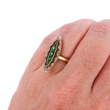 Gold ring with green gemstones on a hand against a white background