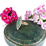 Gold ring with green gemstone on a decorative box with pink flowers