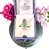 Gold ring with emerald and diamond design in a David Henderson jewelry box with flowers around.
