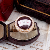Decorative ring with a detailed design in an open jewelry box on a textured surface.