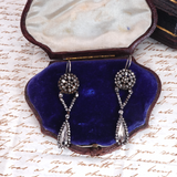 Pair of silver earrings in a blue velvet jewelry box on a piece of paper with text.