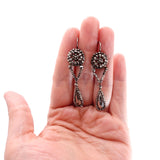 Silver earrings held in a hand against a white background