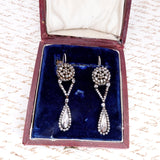 Pair of silver earrings with teardrop design in an open jewelry box on a textured surface.