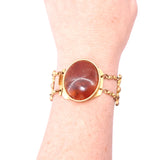Gold bracelet with a large amber stone on a wrist against a white background