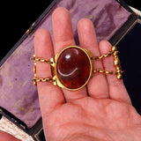 Gold bracelet with a large red stone held in a hand against a dark background