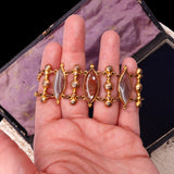 Gold bracelet with gemstones held in a hand against a dark background