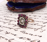Vintage ring with red gemstones and pearls on a piece of paper with cursive writing.