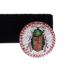 Decorative earring with beetle design on a black stand against a white background