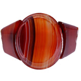 A round signet ring featuring a polished band of agate with natural red, orange, and dark brown banded patterns, set against a plain white background.