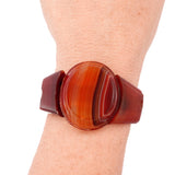 A translucent reddish-brown bangle bracelet with a circular agate-like center and matching side panels, shown worn on a person's wrist against a white background.