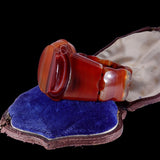 A carved red agate ring displayed on an open vintage velvet jewelry box against a solid black background.