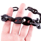 A close-up of a hand holding a black link chain bracelet with oval links and circular cutouts, shown against a plain white background.