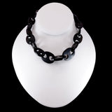 A chunky black resin link necklace displayed on a white neck mannequin against a solid black background.