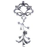 An ornate silver-toned pendant featuring a heart-shaped top with swirling floral details and a dangling vine-like design set with small clear stones, shown on a white background with a faint reflection below.