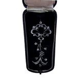 A silver-toned ornate brooch with floral and scroll motifs, displayed inside an open black velvet jewelry box with a cream satin lining.
