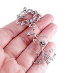A silver-toned floral vine pendant with clear stones, held in the palm of a hand against a white background.