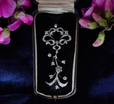 An ornate silver filigree brooch with clear stones, displayed in a black velvet jewelry box with a satin ribbon lid, framed by pink flowers on a dark blue velvet background.