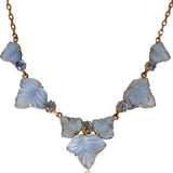 A gold-tone necklace featuring carved light blue mother-of-pearl leaf-shaped beads and small round blue crystals, displayed on a clean white background.