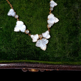 A vintage-style necklace featuring carved white mother-of-pearl butterfly motifs and small clear faceted beads on a gold-tone chain, displayed on a textured green velvet surface.