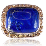 A vintage-style ring featuring a large, square-shaped deep blue lapis lazuli stone in a textured, gold-toned bezel setting, shown on a clean white background with a soft reflection below.