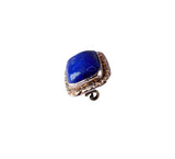A single ring featuring a large, polished blue lapis lazuli stone in a silver-toned bezel setting with small clear stones around the perimeter, shown on a plain white background.