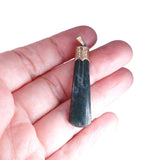 A dark green polished stone pendant with a gold-toned cap and bail, held in the palm of a hand against a white background.