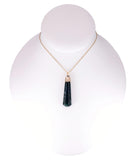 A gold chain necklace with a dark green teardrop-shaped pendant, displayed on a white mannequin bust against a white background.