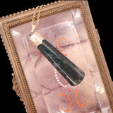 A dark green jade pendant necklace with a gold-toned engraved cap and chain, displayed inside an ornate vintage gold case with a pinkish iridescent lining.