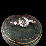 A sterling silver horseshoe-shaped bracelet with floral details, displayed on top of a vintage dark green leather jewelry box with gold trim against a solid black background.