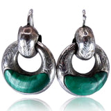 A pair of silver-toned hoop earrings with a cat-head detail on top and a polished green stone inlay along the lower half, shown against a white background with a soft reflection below.