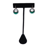 A pair of silver-toned dangle earrings with green circular stone inlays, displayed on a black T-shaped jewelry stand against a white background.