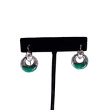 A pair of silver-tone drop earrings with green oval inlays, displayed on a black T-stand against a white background.