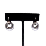 A pair of silver-toned hoop earrings with a polished, reflective finish, displayed on a black velvet T-stand against a solid white background.