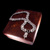 A silver-toned chunky link necklace with a matching pendant, displayed on a dark brown textured book against a solid black background.